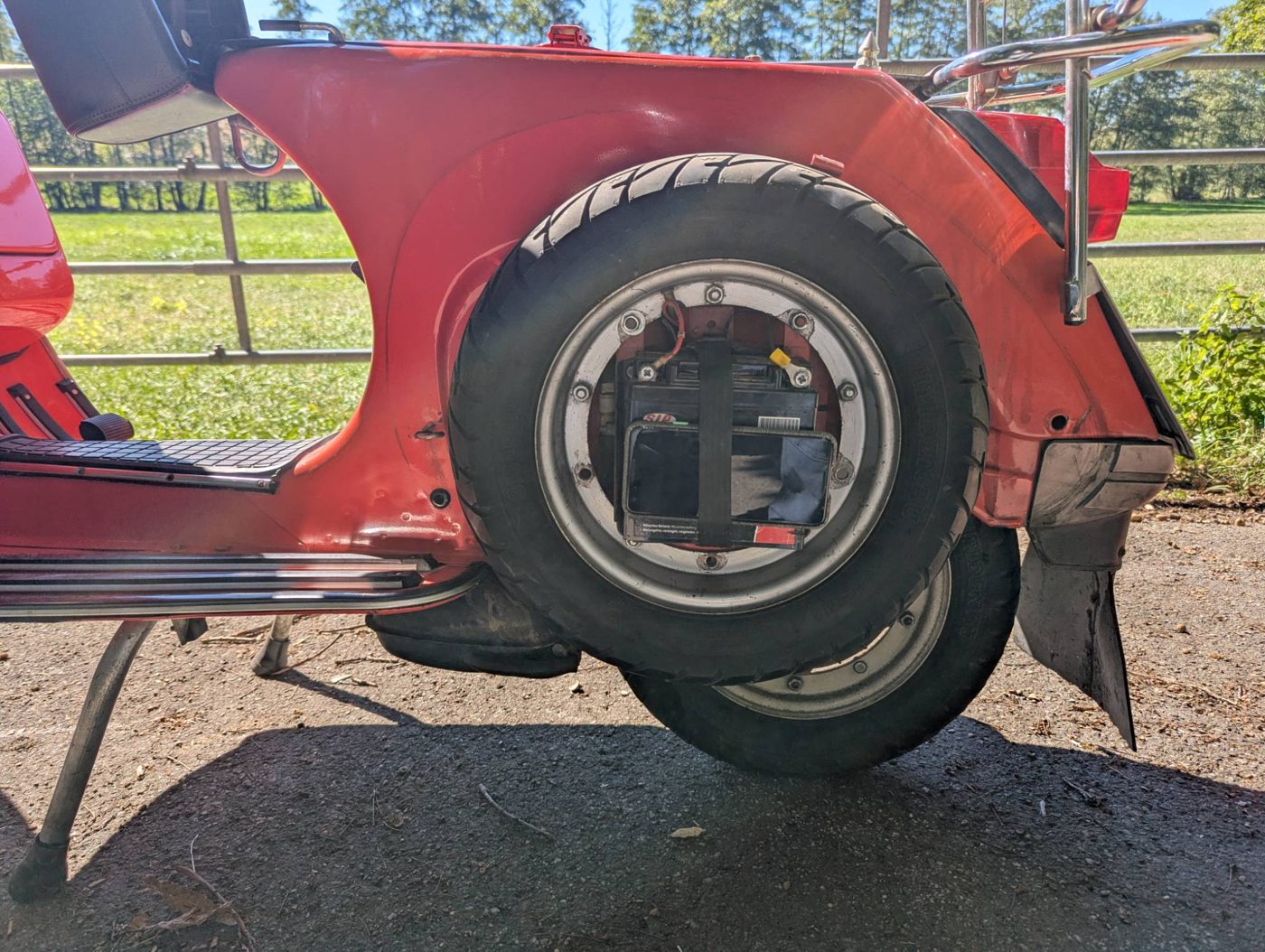 Rote Vespa PX 80 von der Seite. Hinter dem Reserverad ist das Handy mit einem Klettband am Akku befestigt.